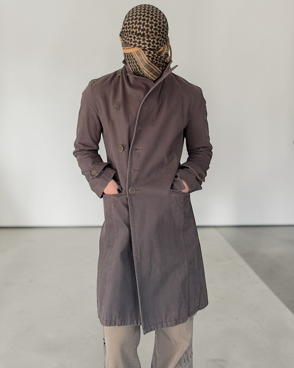 Person wearing a long coat and headscarf in a minimal indoor setting